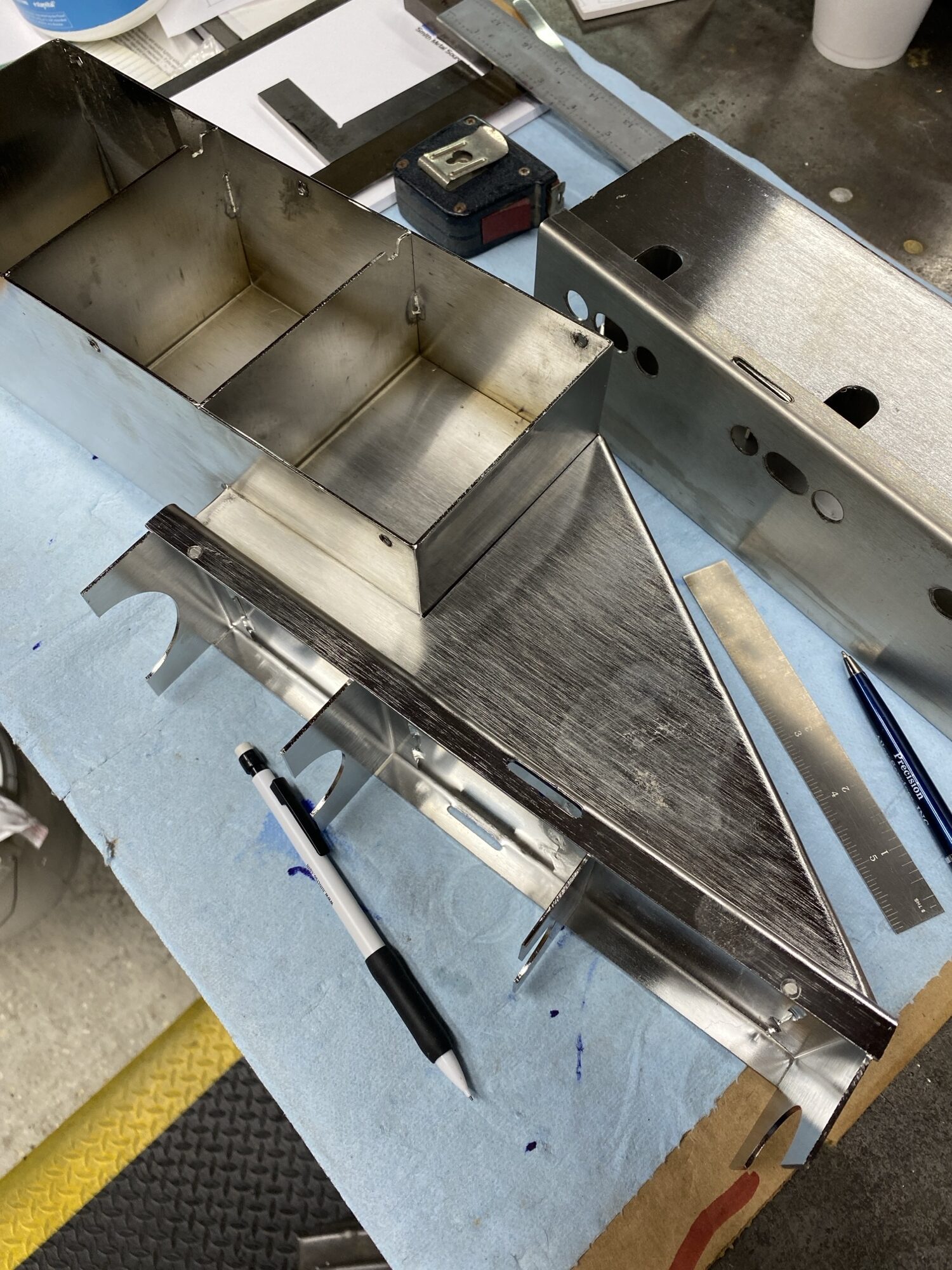 Metal components and tools laid out on a work surface, showcasing a partially assembled metallic structure, emphasizing manufacturing or assembly processes.
