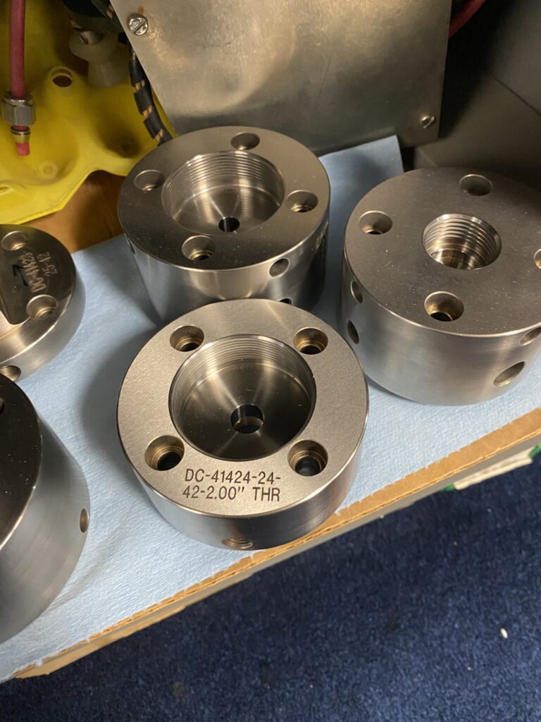 Close-up of several metallic flanges, featuring various holes and marked specifications. These components are likely used in machinery or engineering applications.
