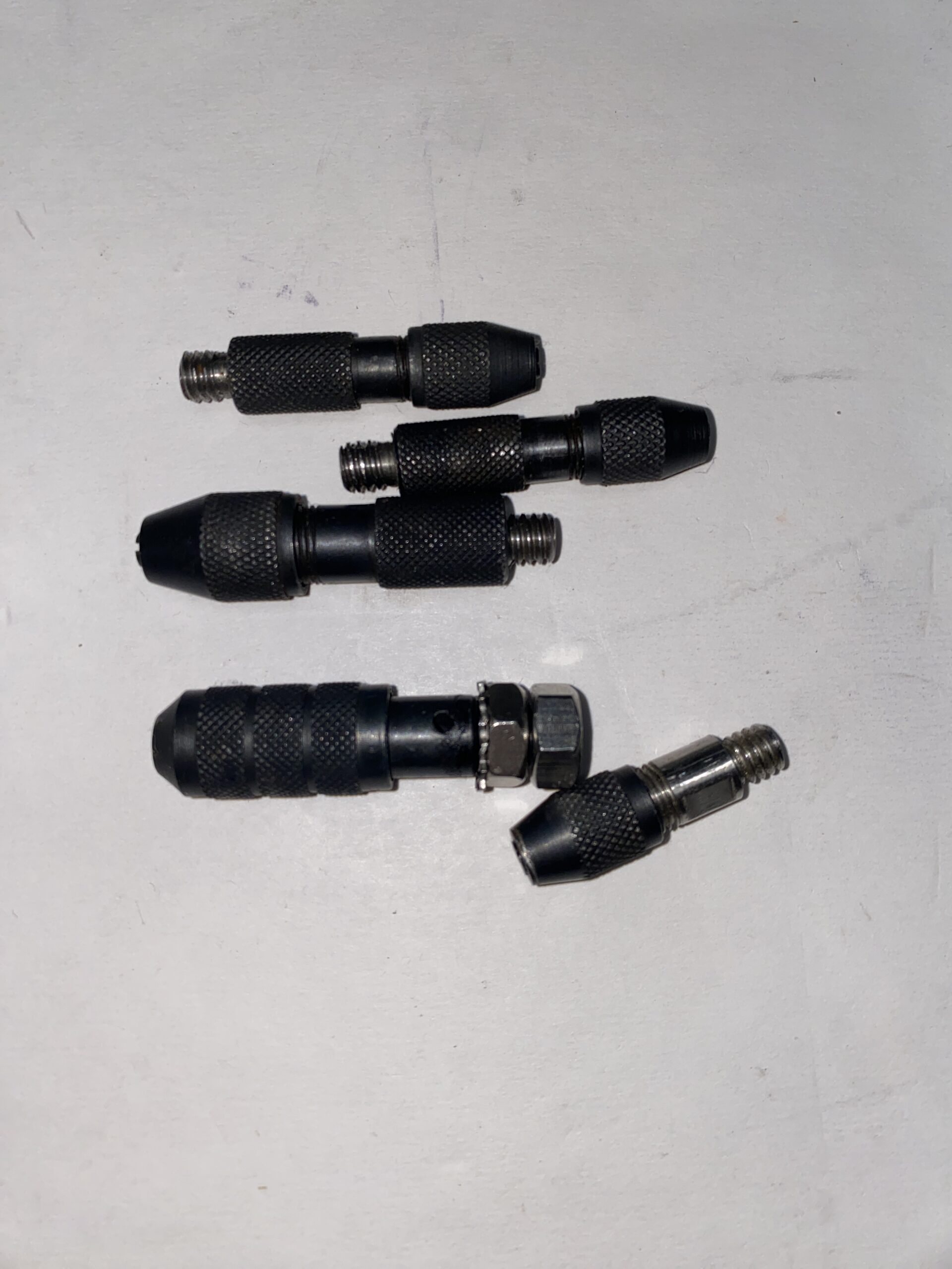 Five black metal connectors with textured grips arranged on a light surface. These are likely used for specific mechanical or plumbing applications.